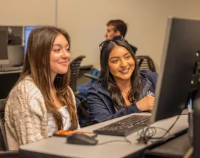 Two girl are smiling and looking in a computer screen