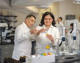 Two people in lab coats are handling a test tube in a laboratory.