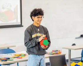 A student holds up a colorful educational toy at the front of a classroom.