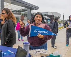 Student holding a CSUMB pennant and smiling at the camera.