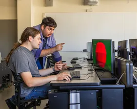 Two people are looking at the screen and pointing at it.