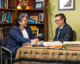 Student smiling with the professor while holding a pencil and books in the background.