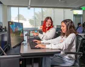 CSUMB communication design students work together at a computer workstation, discussing and refining a digital design project.