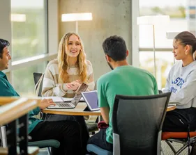 A group of four students sitting around a table and talking