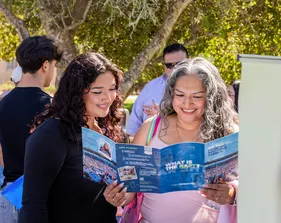Student and parent smiling while looking at a CSUMB brochure.