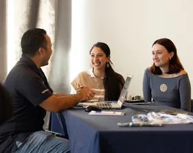 3 students sitting at a table with laptops