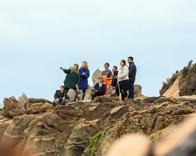 Marine science students gather on a rocky coastal outcrop during a field study, observing the shoreline and engaging in hands-on research within the natural environment near Monterey Bay at Cal State Monterey Bay.