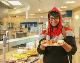 A student holds up a plate of food with in the dinning commons.