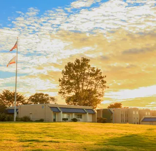 A campus with buildings and flagpole at sunset on a grassy field.