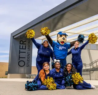The campus mascot and cheer team pose outside the Otter Student Union, celebrating school spirit and community pride.