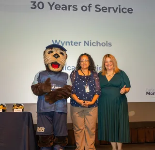 Women posing with the Mascot on the stage