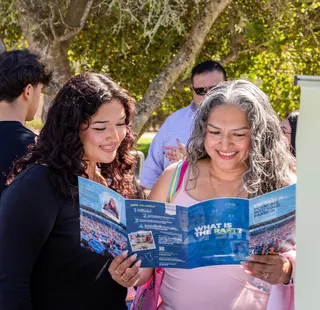 Student and parent smiling while looking at a ���ӽ紫ý brochure.