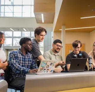 Group of students collaborating on a computer in the Business and Information Science building.