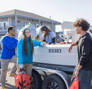 A group of four students standing next to a boat