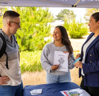Two people showing a student a social work flyer while smiling and pointing at it.