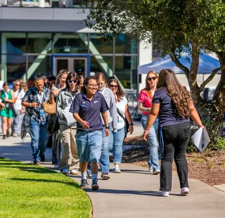 A group of people walk together outdoors on a sunny day, smiling and chatting as they take part in a campus or community event.