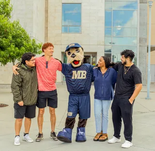 Students standing with the Mascot in front of the building