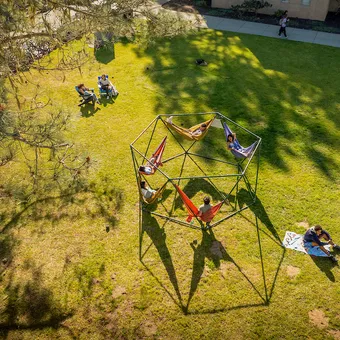 Students sitting on hammock structure, blankets, and chairs in a grassy quad