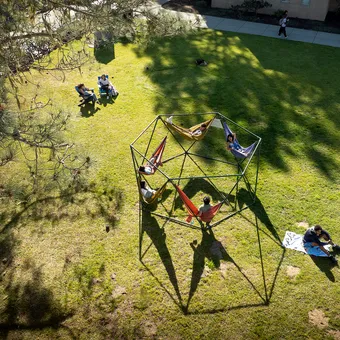 Students sitting on hammock structure, blankets, and chairs in a grassy quad