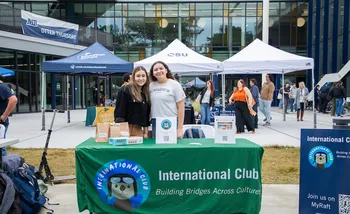 two students posing and smiling in front of a table for the International Otters Club