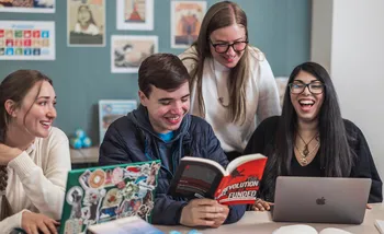 CSUMB Global Studies students laugh and discuss ideas while reading books and using laptops together during a collaborative classroom study session.