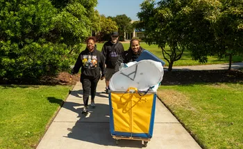 Male student pushing Move In cart with supporters on CSUMB quad