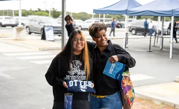 Two people smiling under a tent, holding an T-shirt and a flyer.