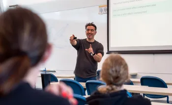 Instructor gesturing while teaching a class in a classroom.