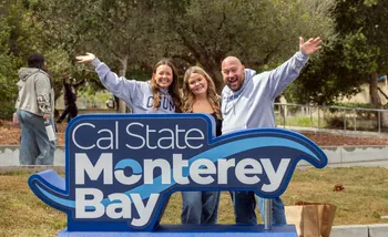 New student with their family in front of CSUMB logo signage.