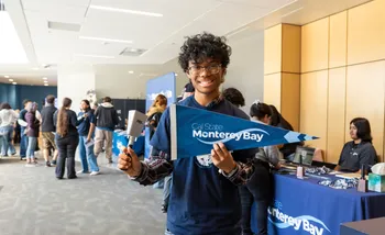 New student holding CSUMB pennant and cowbell.
