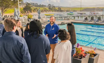 Faculty member standing in front of a pool talking to a group of hospitality students.