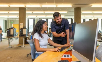 Student getting advise while seated at computer in library
