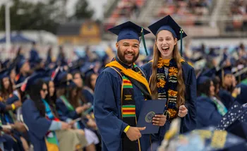 Two CSUMB Grads smiling while holding diplomas