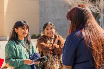 Community members connect with a staff member outdoors, sharing information and building relationships in a welcoming campus setting.