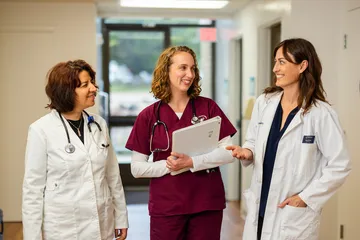 A nursing student in a scrub and two professors standing in a walkway talking together