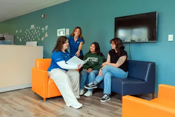 CSUMB housing staff members sit with two students in a lounge area, reviewing information together on a binder inside the Student Housing and Residential Life office.