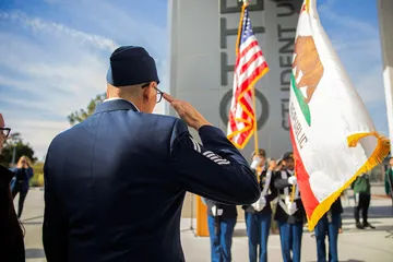 A uniformed service member salutes during a campus ceremony, honoring service and tradition in a formal setting.
