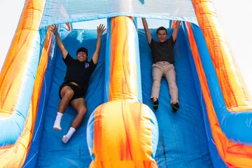 Two students race down a large inflatable slide during a campus recreation event at Cal State �鶹��, smiling with their arms raised in celebration.