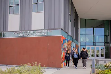 A group of people is walking near a CAHSS building. Just behind them is a painted wall.