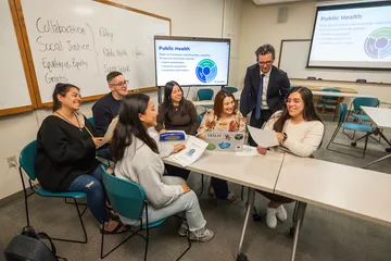 Student showing a paper to a professor while other students listen.