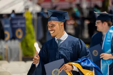 A student in cap and gown holding a diploma in his hand