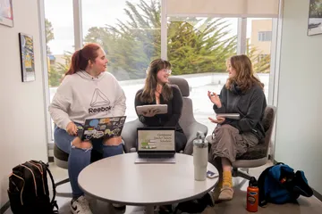Three students collaberating together on group work discussing.