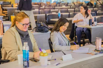 Students at California State University, Monterey Bay (CSUMB) take notes and engage during a classroom or workshop session in a modern lecture hall. The atmosphere is collaborative and professional, emphasizing active learning and participation.
