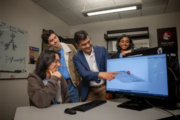 Three students looking at a computer while the professor points at it smiling.