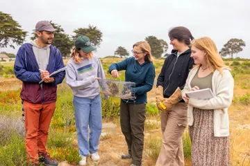 A group of four AES students and a professor standing in the grass while the professor is holding a squirrel in a cage