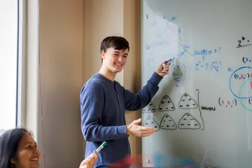 A statistics student writing on a whiteboard