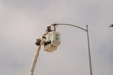 A facilities staff member repairs a CSUMB streetlight while elevated in a bucket lift, demonstrating ongoing infrastructure maintenance.