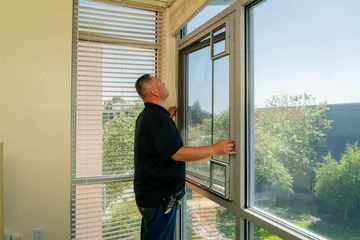 A technician checks a window latch and frame inside a residence hall, inspecting for safety and operability.
