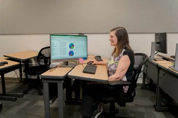A finance team member at CSUMB works independently at a desktop computer, analyzing charts and data in a spreadsheet during a quiet training session.