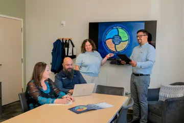 A small group of CSUMB HR team members meet in a conference room, reviewing a values-based strategic framework displayed on a large screen during a planning session.